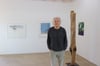 Gastgeber Werner Schlegel steht neben einer Holzskulptur von Matthias Heß, die an einen menschlichen Torso erinnert. Schlegel kombiniert Skulpturen im Raum mit Bildern an den Wänden.