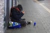 Eine obdachlose Person sitzt zu später Stunde in der Kälte und Nässe auf dem Boden.