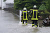 Feuerwehrleute waten in Dasing im schwäbischen Landkreis Aichach-Friedberg durch eine überflutete Straße.